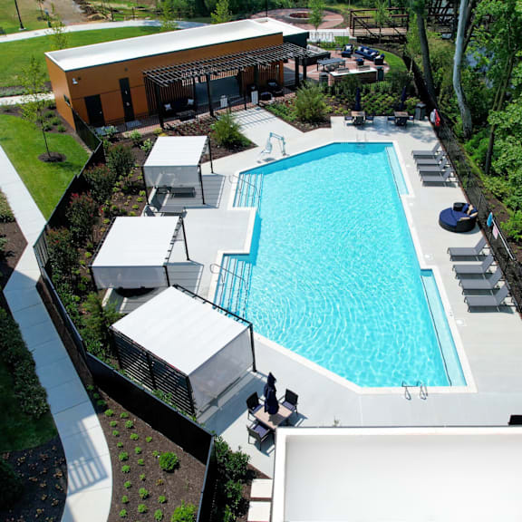 a sparkling resort-style pool near trees with lounge chairs, tables, chairs, and 3 shaded lounge areas.