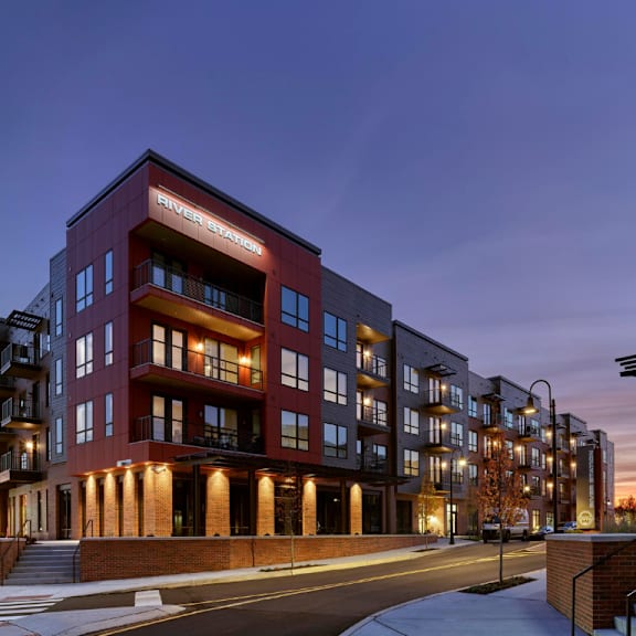 a corner street view of river station's apartment buildings at sunset with trees and the capitol building in the background.