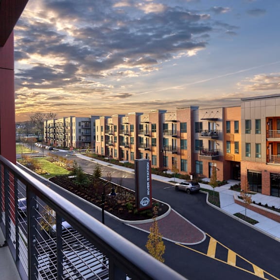 a balcony view of river station's modern apartment building lining a street with the sun setting in the background.
