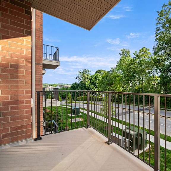 a balcony with a metal railing overlooks a street and greenery.