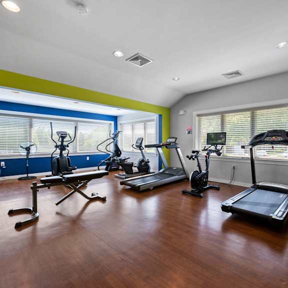 a spacious fitness center with beautiful hardwood flooring, large windows, cardio and weight equipment, a filtered water station, and large windows.