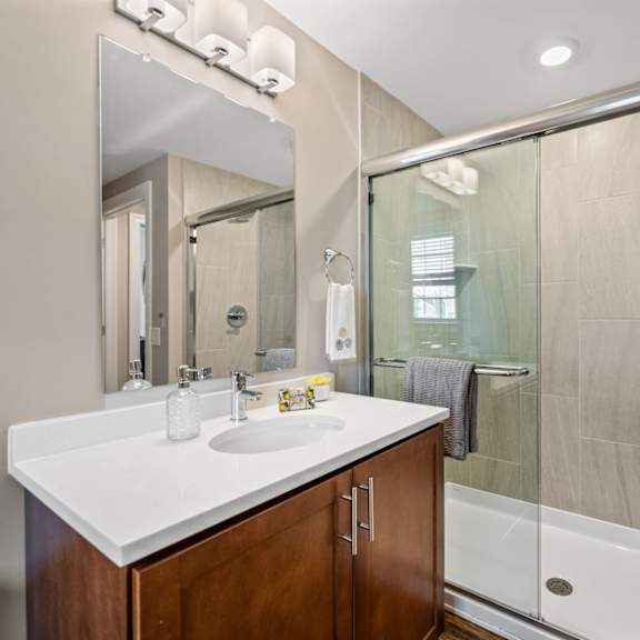 a bathroom inside an exton apartment with vanity, large mirror, and sliding glass doors leading to a stand-up shower with tile walls.