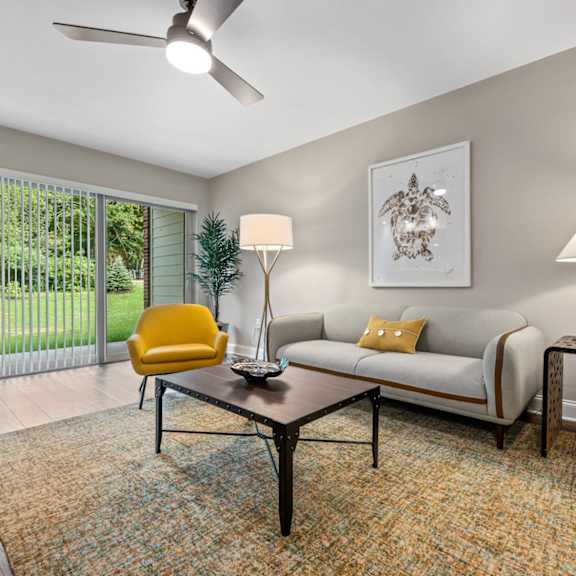 a living room with hardwood-style flooring, ceiling fan, and large sliding glass doors to private patio with well-maintained green space.