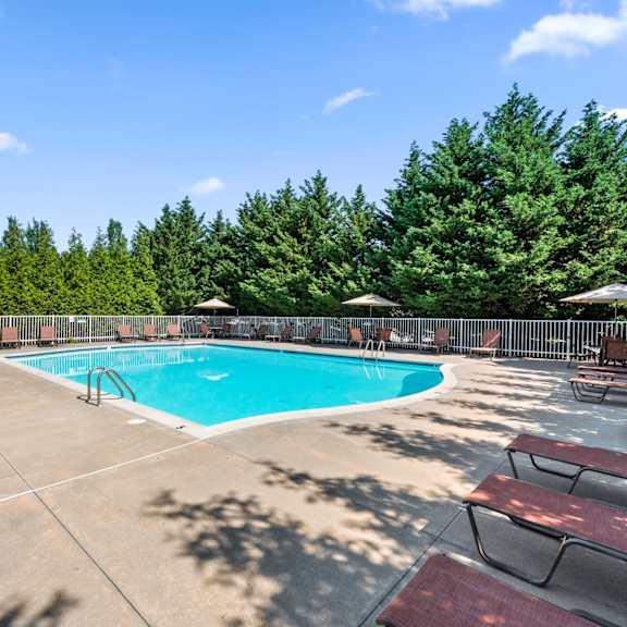 a gated resort-style pool with lounge chairs, tables with umbrellas, and a sundeck at severgn apartments.