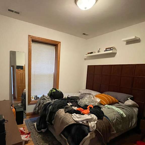 a bedroom with a messy bed and a window with blinds.