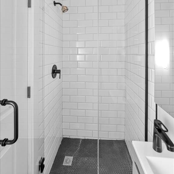 a white tiled bathroom with a black shower head and a black and white shower curtain.