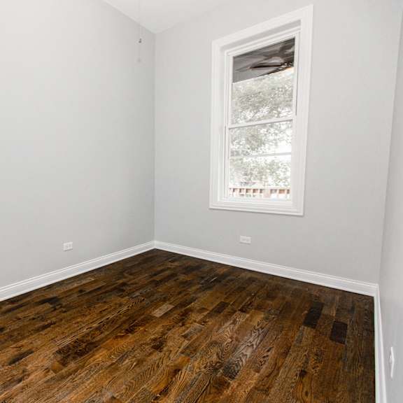 an empty room with wooden floors and two windows