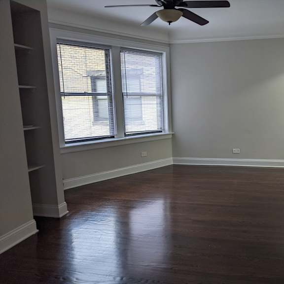 a room with a ceiling fan and two windows.