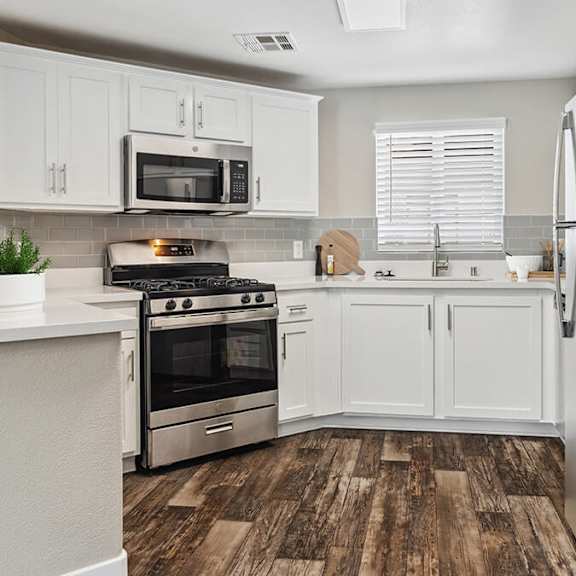 model kitchen with white cabinets and wood-style flooring at reserve at rancho apartments located in moreno valley, ca.