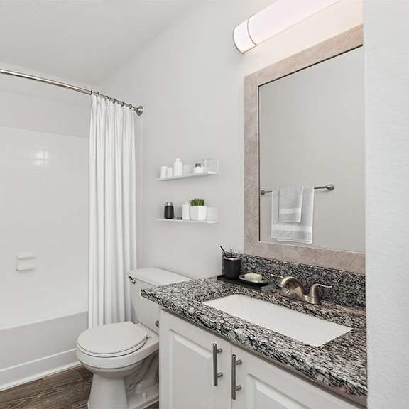 model bathroom with white cabinets and wood-style flooring at seven lakes at carrollwood apartments in tampa, fl.