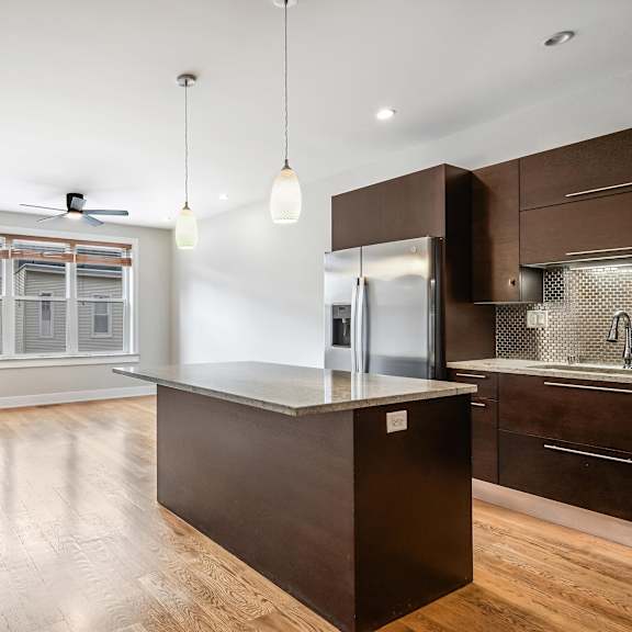 a modern kitchen with a dark brown island and wooden floors.