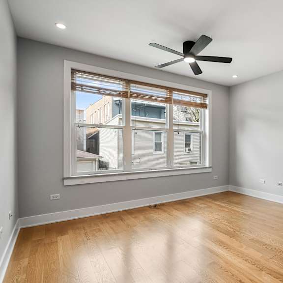 a room with a ceiling fan and a window overlooking a building.