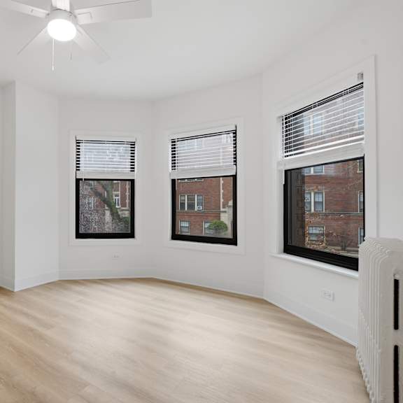 a room with a ceiling fan and three windows.