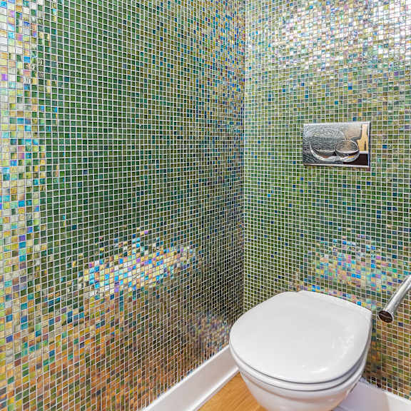 a white toilet in a bathroom with a mosaic tile wall.