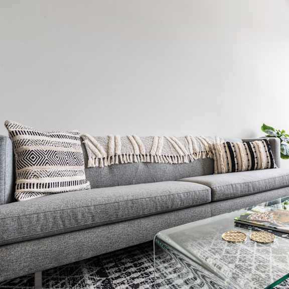 a living room with grey couches, a glass coffee table, and large window 