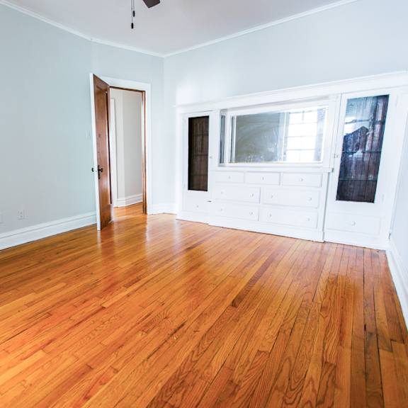 an empty living room with wood floors and a door to a bedroom