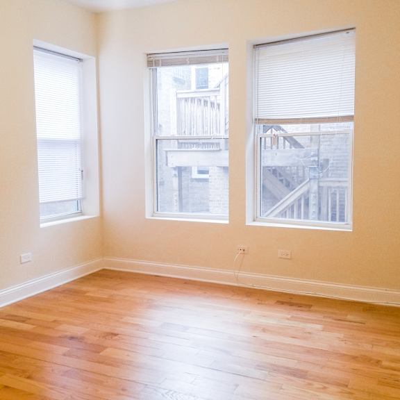 an empty living room with wood floors and three windows