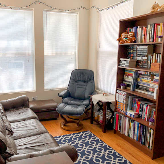 a living room with a brown leather couch, a blue chair, and a bookshelf filled with books.