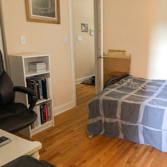 a bedroom with a bed, chair, and a bookshelf.