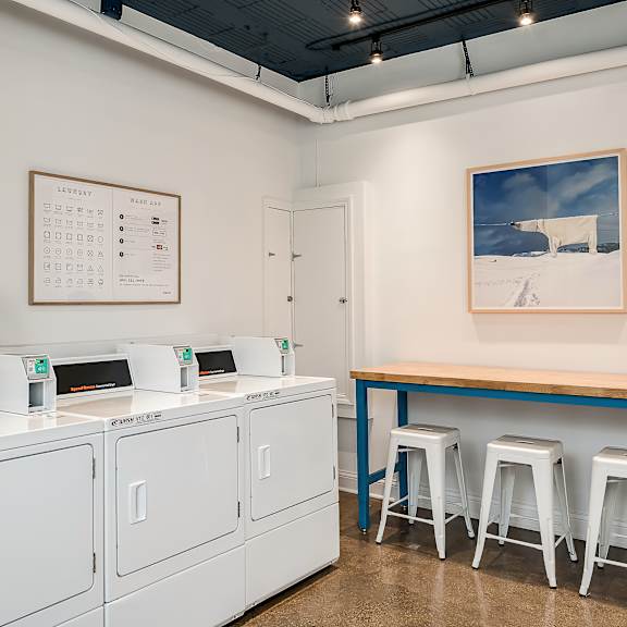 a laundry room with three washing machines and a counter with three stools