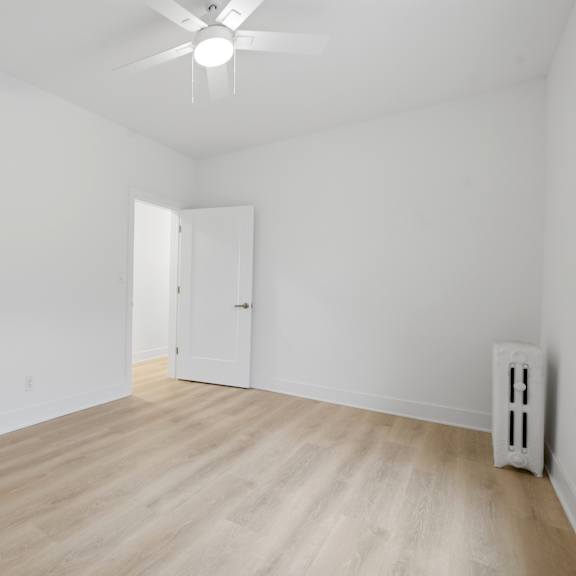 a room with white walls and wooden flooring with a ceiling fan.