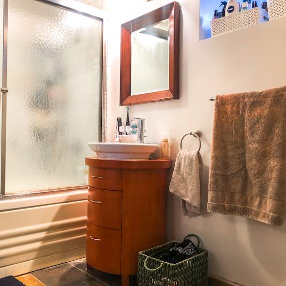 a bathroom with a brown cabinet, a mirror, and a window with towels hanging on the wall.
