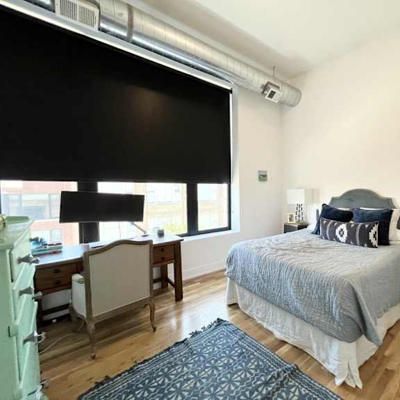a bedroom with a bed, desk, chair, and window.