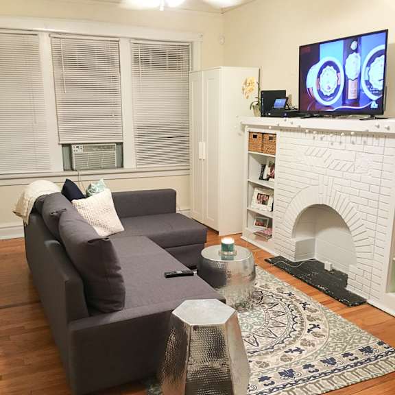 a grey couch with a white pillow and a tv on the wall.