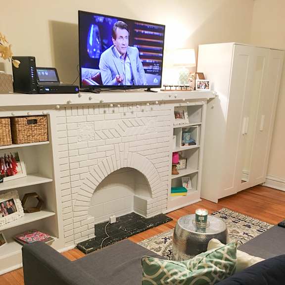 a grey couch with a green pillow is in front of a white fireplace.