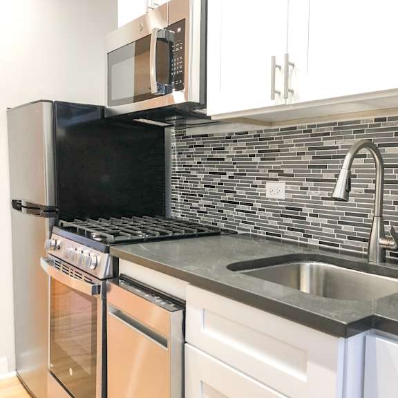 a kitchen with a black microwave above a stove and a silver sink.