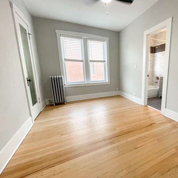 a room with wooden flooring and a window with blinds.