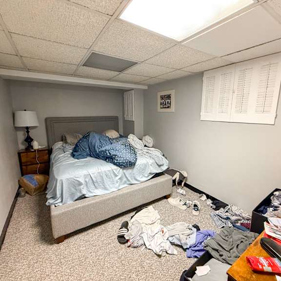 a messy bedroom with a bed, dresser, and clothes scattered on the floor.