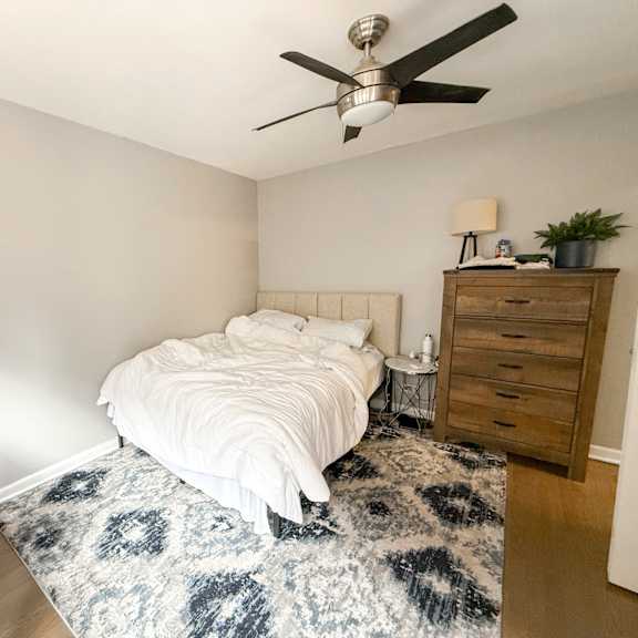 a bedroom with a bed, a dresser, a ceiling fan, and a rug.