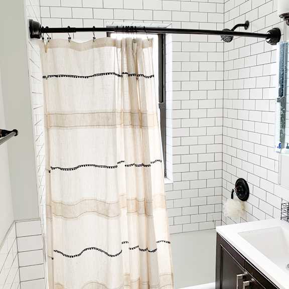a white shower curtain with black lines hangs in a white tiled shower.