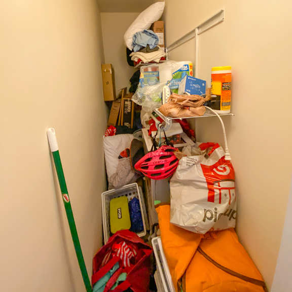 a small, narrow hallway is filled with various items, including a mop, bags, and boxes.
