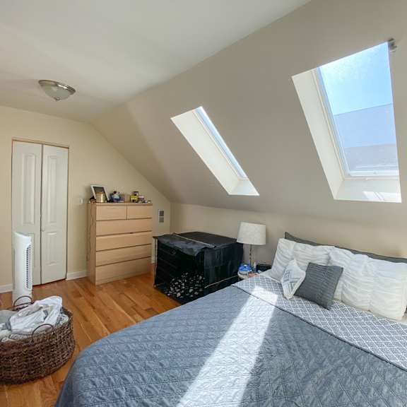 a bedroom with a bed, nightstand, and a window with skylights.