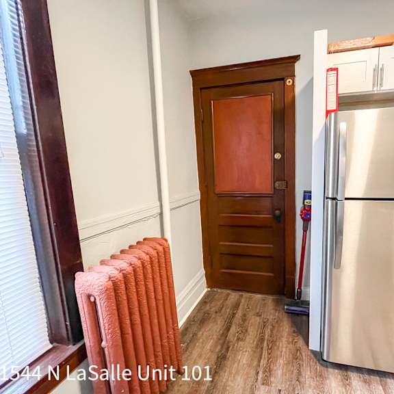 a kitchen with a refrigerator, a red mop and a brown door.