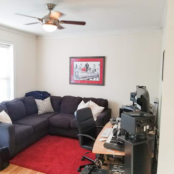 a living room with a grey couch, a red rug, and a ceiling fan.