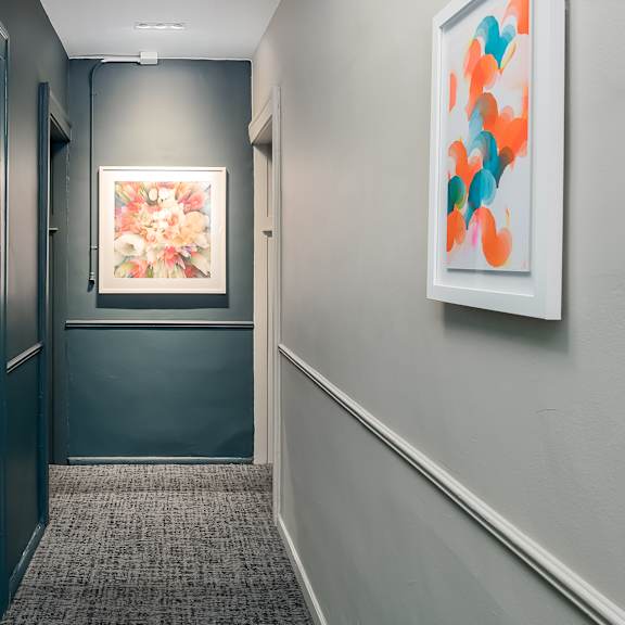 a hallway with a painting on the wall and a carpeted floor.