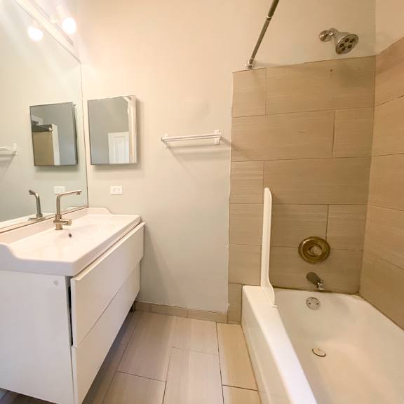 a white bathroom with a sink, mirror, and bathtub.