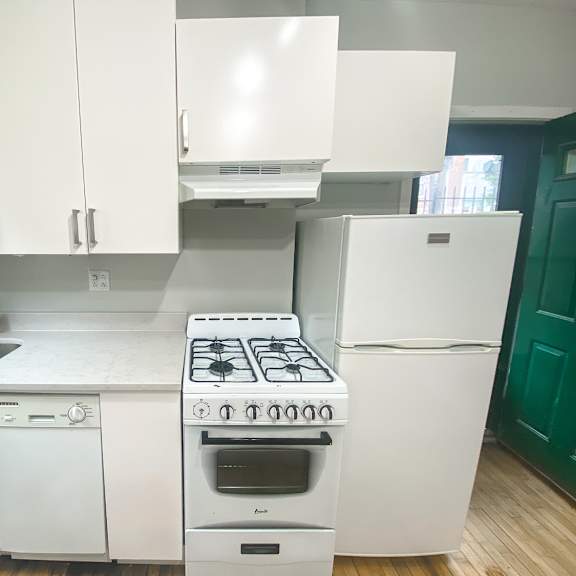 a white kitchen with a stove, sink, and cabinets.