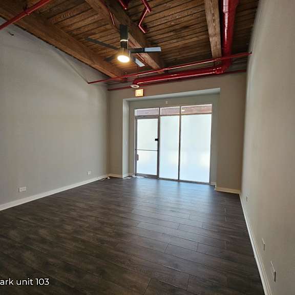 an empty living room with wood floors and a door to the kitchen