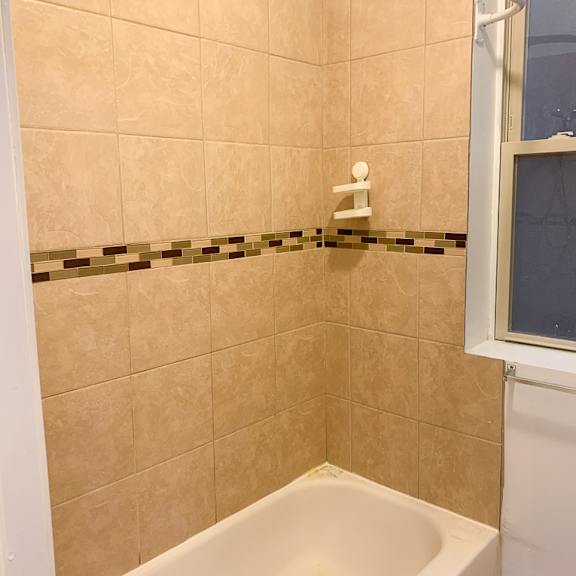 a white bathtub in a bathroom with beige tiles.