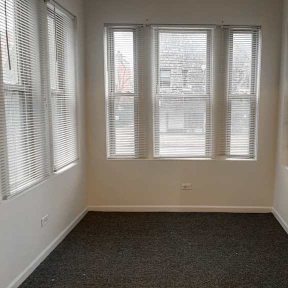 a room with a carpeted floor and three windows covered with blinds.