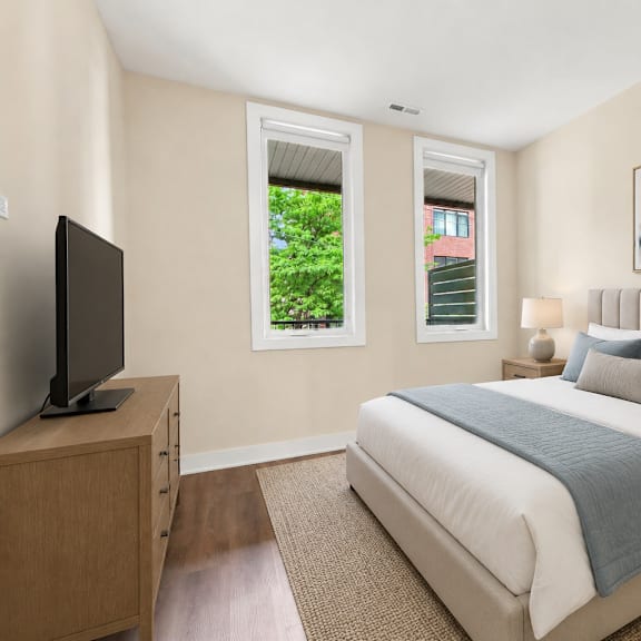 a bedroom with a large bed, a television, and a window with a view of trees and a building outside.