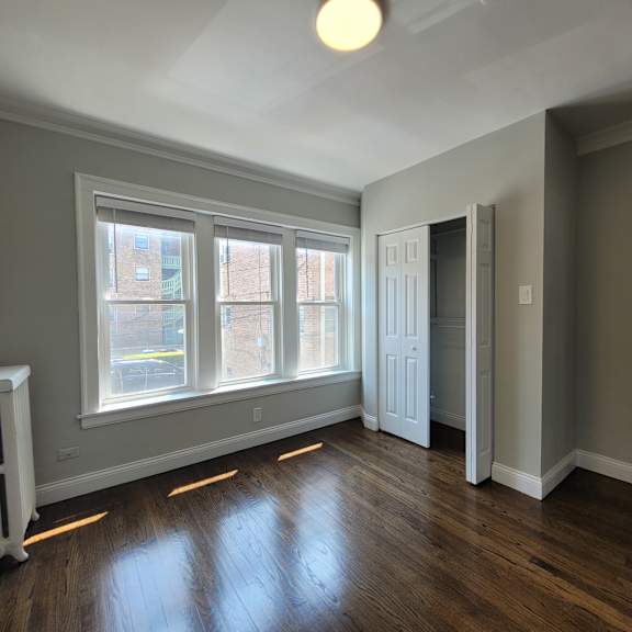 a room with a wood floor and a window with a view of a building across the street.