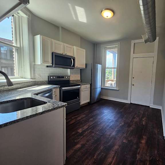 a kitchen with dark wood floors and white cabinets.