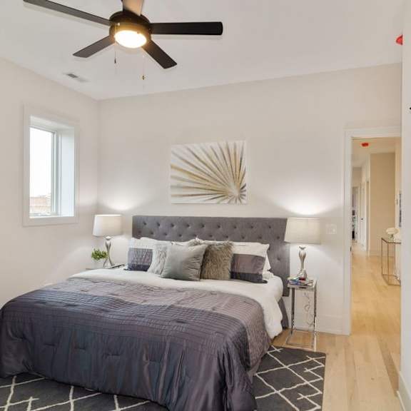 a bedroom with a bed, pillows, a ceiling fan, and a wall art piece.