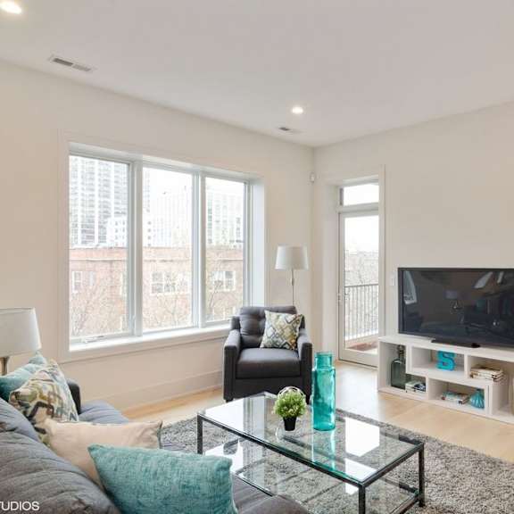 a living room with a grey couch, a black chair, a glass coffee table and a television.
