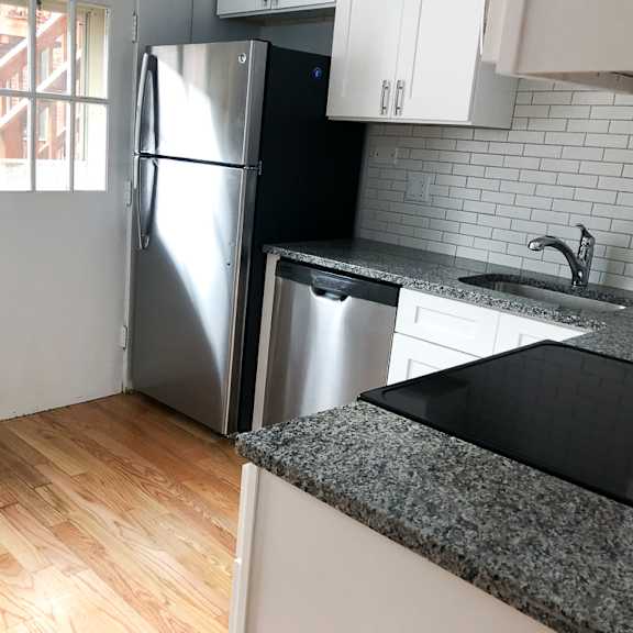 a kitchen with a stainless steel refrigerator and a black granite countertop.